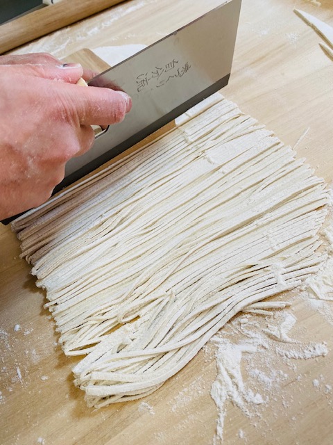 伸ばしたそば粉を真剣に切る旦那さん